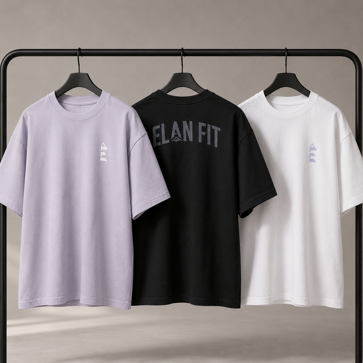 Drei ÈlanFit Oversized T-Shirts in Lavendel, Schwarz und Weiß auf einem Kleiderständer